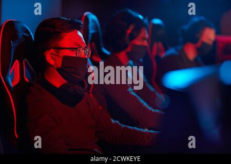 Group of computer programmers in protective masks using computers in their work in dark office Stock Photo