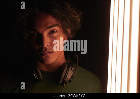 Portrait of young gamer in headphones looking at camera standing in dark room near the lighting equipment Stock Photo