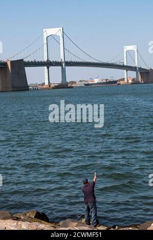 A lone fisherman fishes in Little Bay Park with the Throgs Neck Bridge in view in the background. In Whitestone, Queens, New York City. Stock Photo