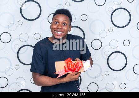 excited young black man holding an enveloped wrapped with a ribbon containing some cash, feeling excited Stock Photo