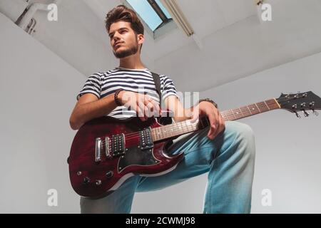 studio portrait from below upward of young guitarist pose with leg up,  holding guitar while looking away Stock Photo - Alamy