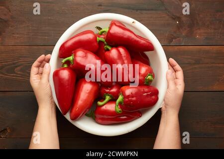 female hands holding a large white plastic bowl with red pepper, top view Stock Photo