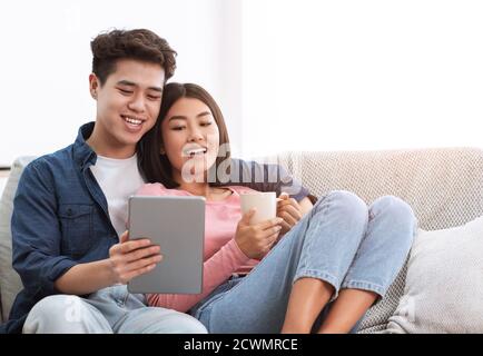 Happy Chinese Couple Using Digital Tablet Relaxing At Home Stock Photo