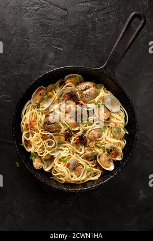 Pasta Spaghetti alle Vongole Seafood pasta with dried tomatoes and leek in black frying pan on black background top view copy space Stock Photo