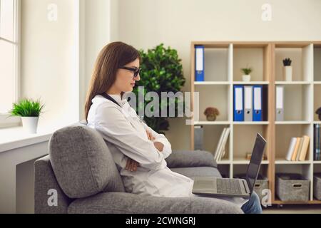Woman doctor therapist sitting in medical clinic and looking at laptop during online meeting Stock Photo