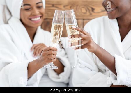 Happy girlfriends in bathrobes sitting on bed and drinking champagne Stock Photo