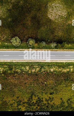 Empty asphalt road through countryside, aerial view from drone pov, Top view roadway as conceptual background for traveling and car insurance themes. Stock Photo