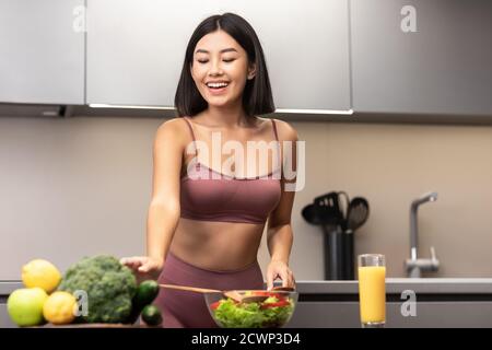 Asian Woman In Fitwear Cooking Salad For Dinner In Kitchen Stock Photo