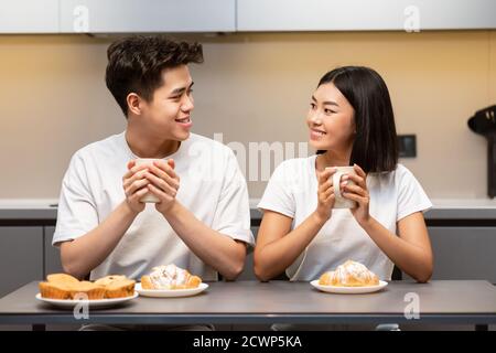 Asian Couple Having Breakfast Sitting In Kitchen On Weekend Morning Stock Photo