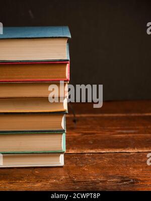 stack of multi-colored books on old wooden shelf with dark background Stock Photo