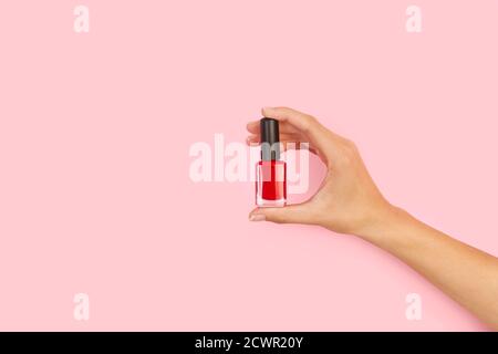 Woman hand holding a red nail polish on a pink background with copy space Stock Photo