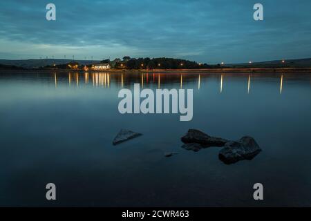 Hollingworth Lake taken during the blue hour with warmth provided by the lights from 'The Wine Press' and the streetlamps reflecting on the water Stock Photo