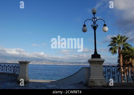 Panoramic sea view of Strait of Messina from Reggio Calabria with Palms iand vintage street lamps in foreground Stock Photo