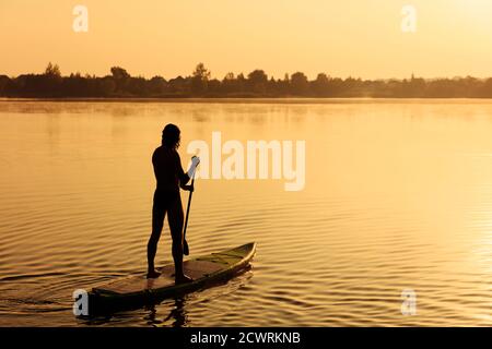 Back view of young guy practicing in swimming on sup board Stock Photo