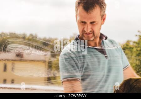 A middle aged man cleaning window with a rag and a window cleaner Stock Photo