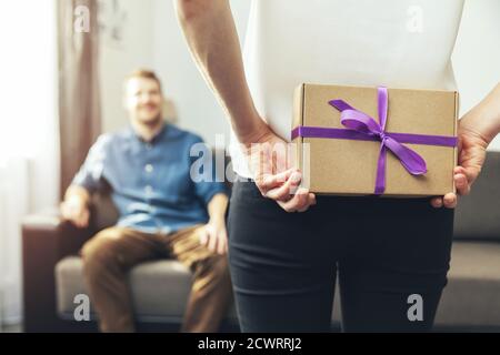 woman hiding surprise present behind back to beloved man at home Stock Photo