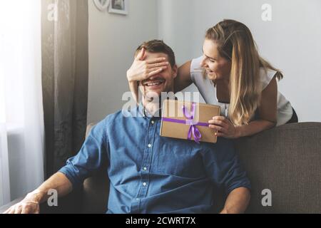 woman giving surprise gift to beloved man at home. closed eyes with hand from behind Stock Photo