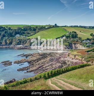 A view of Talland Bay at low tide from up above on the coastal cliff top path on a beautiful early autumn day. Famous for it's pink purple rock strata Stock Photo