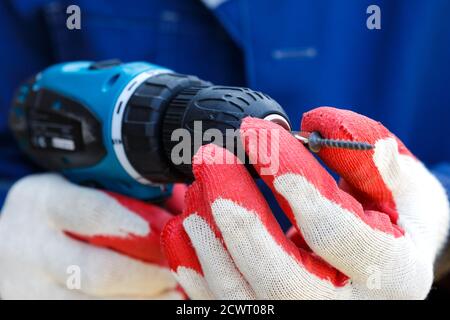 Electric screwdriver in the hands of a carpenter. Male hands in work gloves hold an electric screwdriver. Stock Photo