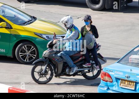 SAMUT PRAKAN, THAILAND, JUL 01 2020, A taxi driver on a motorcycle rides with a woman and her bag. The mototaxi driver carry a passenger between cars Stock Photo