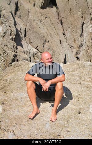 Man in swimsuit sitting on the rock. Stock Photo