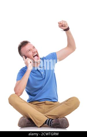 casual young man sitting on the floor with his legs crossed and talking on the phone while cheering and looking up, away from the camera. isolated on Stock Photo