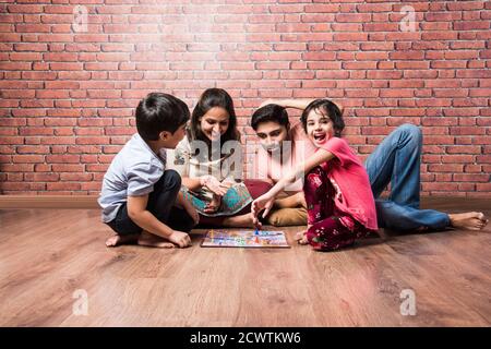Indian young family of four playing board games like Chess, Ludo or Snack and Ladder at home in quarantine Stock Photo