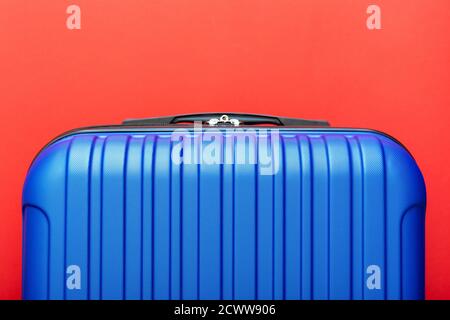 Modern blue suitcase on red background close up with copy space for text. Minimal style travel concept. Vacation trip. Summer holiday stock photo Stock Photo