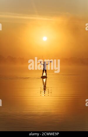 Silhouette of strong man paddling on sup board at foggy lake Stock Photo