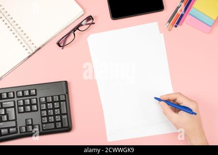 White clean sheets for records, hand holds pen, office glasses on a pink background. Flat lay. Office content. pink table Stock Photo