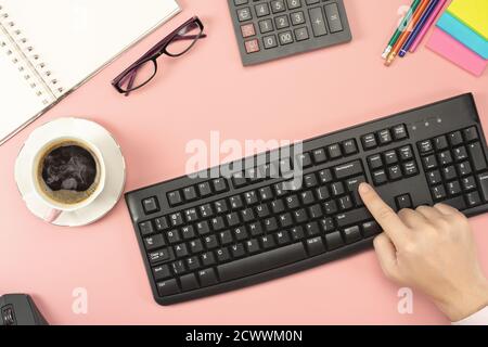Man sitting at a pink office Desk presses the enter button on the keyboard. Flat lay, top view office table desk Stock Photo