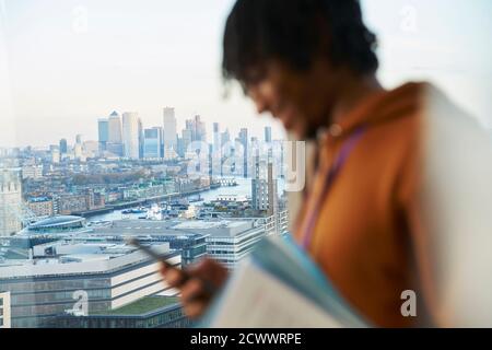 Businessman using smart phone at highrise window, London, UK Stock Photo