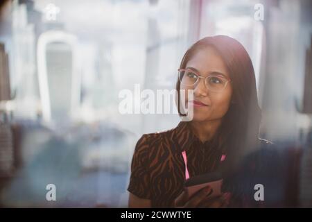 Thoughtful businesswoman with smart phone in sunny window Stock Photo