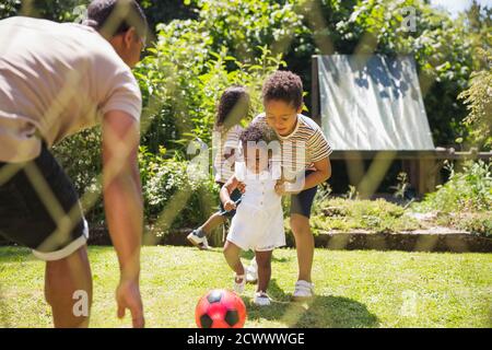 Family playing soccer in sunny summer backyard Stock Photo