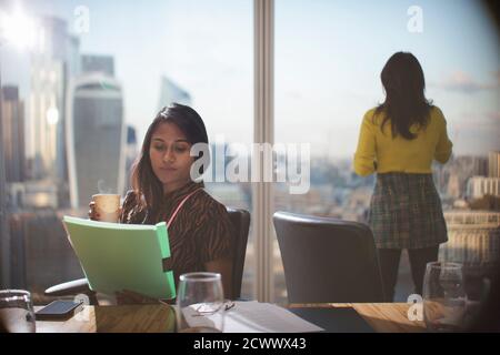 Businesswoman with coffee reviewing paperwork in conference room Stock Photo