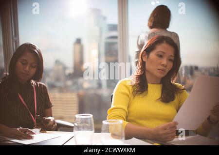 Businesswomen reviewing paperwork in highrise conference room meeting