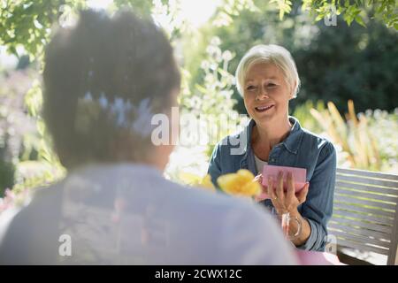 Happy senior woman opening gift from husband on sunny summer patio