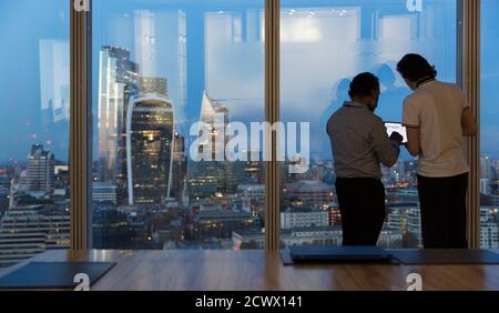 Businessmen working late at highrise office window, London, UK Stock Photo
