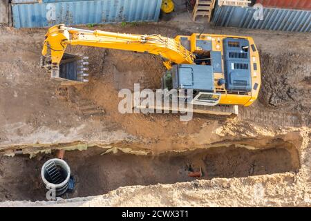 Excavator at a construction site while digging trenches for calcining sewer and drainpipes with a raised bucket, top aerial view Stock Photo