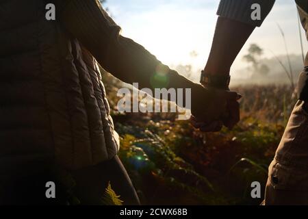Close up silhouette young couple holding hands on sunny hike in nature Stock Photo