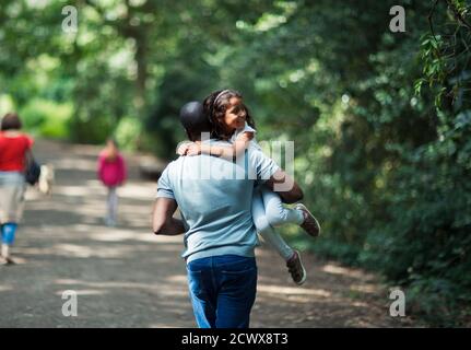 Playful father carrying happy daughter on trail in woods