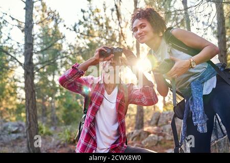 Curious young hiker couple using binoculars and camera in sunny woods Stock Photo