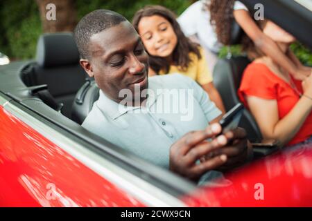 Man using smart phone in convertible with family Stock Photo