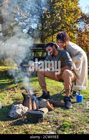 Happy young couple enjoying campfire in sunny autumn field Stock Photo