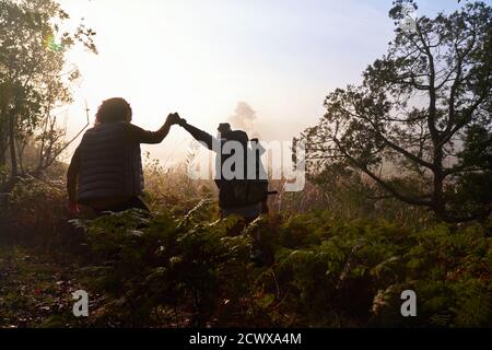 Silhouette young couple holding hands hiking in woods at dawn Stock Photo