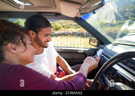 Young couple using smart phone on road trip in sunny car Stock Photo