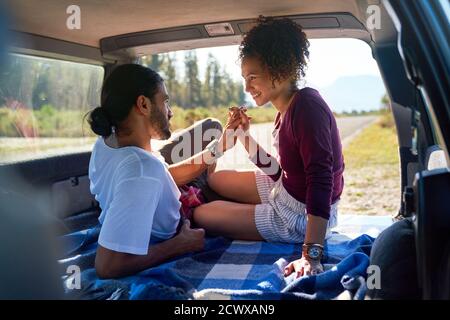 Happy affectionate young couple holding hands in back of sunny car Stock Photo