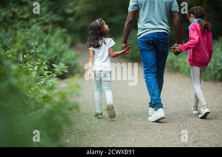 Father and daughters holding hands walking on path in park