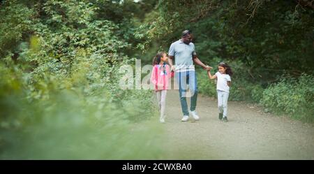 Father and daughters holding hands on path in park Stock Photo