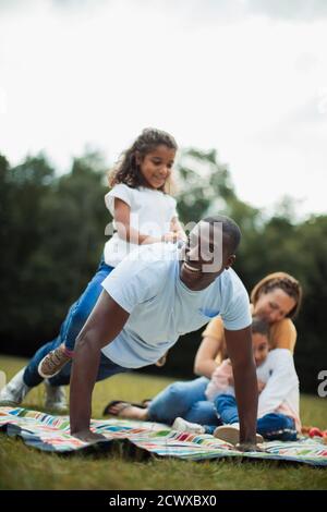 Playful father doing push ups with daughter on back in park Stock Photo
